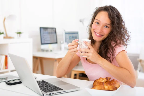 Jovem estudante atraente tomando café da manhã enquanto trabalhava — Fotografia de Stock