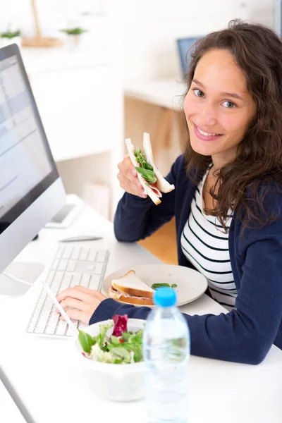 Jonge aantrekkelijke student eten boterham terwijl u werkt — Stockfoto