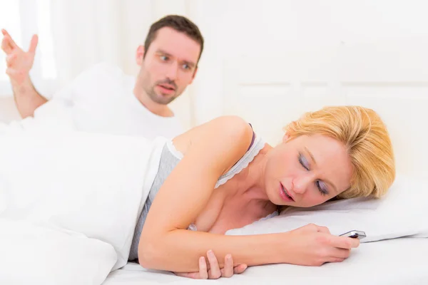 Casal jovem que discute em uma cama a causa de textos — Fotografia de Stock