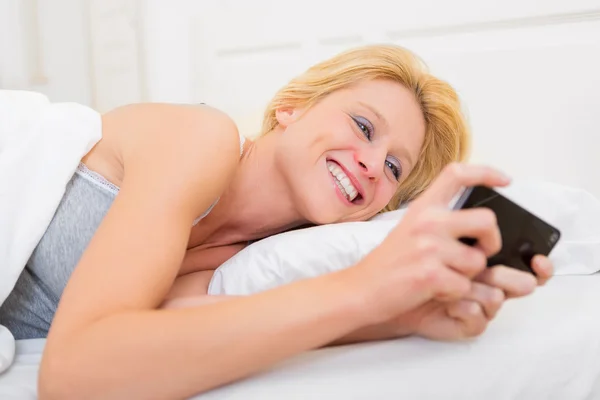 Junge attraktive Frau sendet Text in einem Bett — Stockfoto