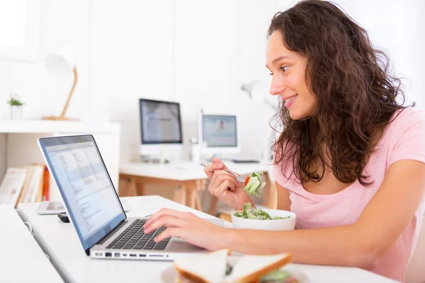 Joven estudiante atractivo comiendo ensalada mientras trabaja —  Fotos de Stock