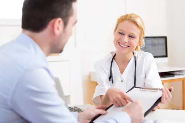 Patient signing the document of a young attractive doctor — Stock Photo, Image