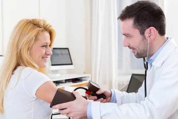 Молодой привлекательный врач проверяет кровяное давление пациента — стоковое фото