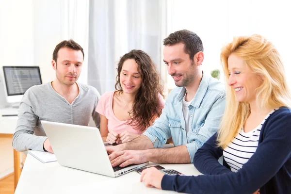 Grupo de 4 jóvenes atractivos trabajando en un ordenador portátil —  Fotos de Stock