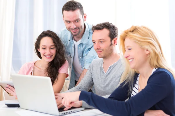 Grupo de 4 jóvenes atractivos trabajando en un ordenador portátil —  Fotos de Stock