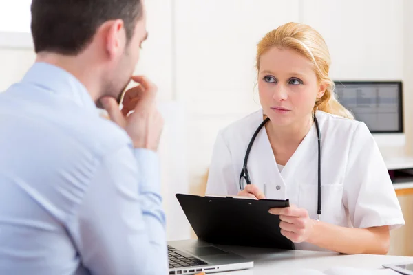 Young attractive doctor taking notes while patient speaking Stock Photo