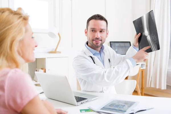 Jovem médico atraente analisando raio-X com paciente — Fotografia de Stock