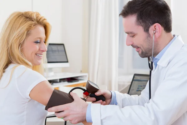 Joven médico atractivo comprobando la presión arterial del paciente — Foto de Stock