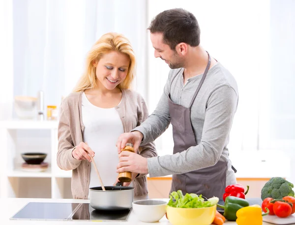 Jovem homem atraente ajudando sua esposa enquanto cozinha — Fotografia de Stock