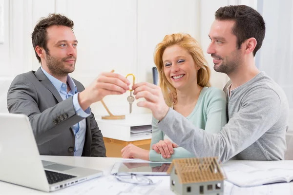 Real estate agent delivers keys of new house to young couple — Stock Photo, Image