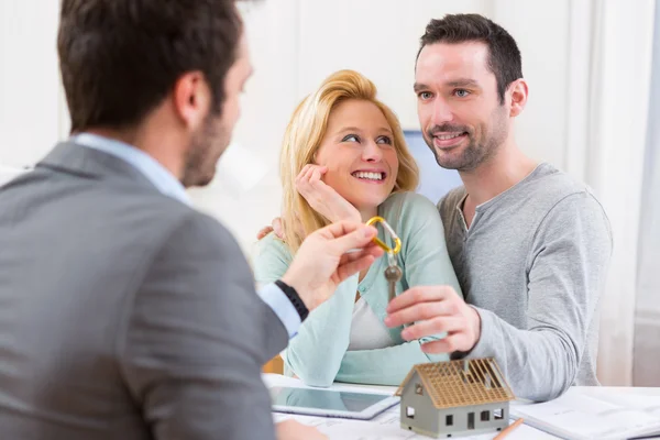 Onroerende goederenagent levert sleutels van nieuw huis aan jong koppel — Stockfoto