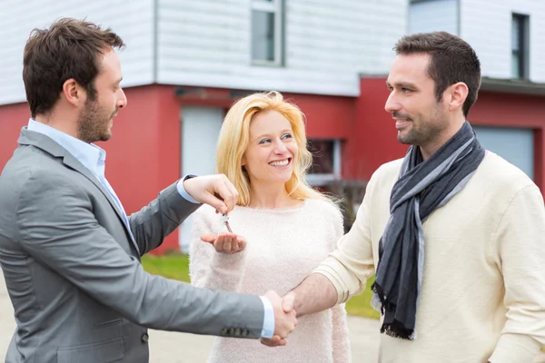 Real estate agent delivers keys to young atractive couple — Stock Photo, Image