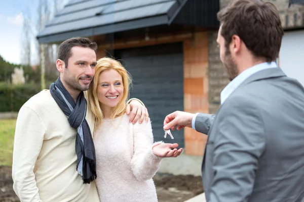 Real estate agent delivers keys to young atractive couple — Stock Photo, Image