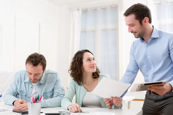 Dos pasantes trabajando juntos asistidos por su supervisor del curso — Foto de Stock