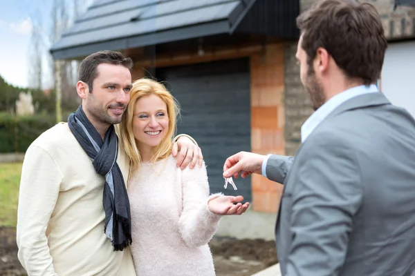 Real estate agent delivers keys to young atractive couple Royalty Free Stock Photos