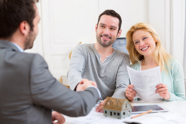 Молодая счастливая пара пожимает руку агенту по недвижимости после подписания С
