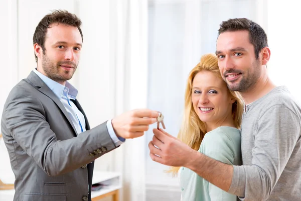 Onroerende goederenagent levert sleutels van nieuw huis aan jong koppel — Stockfoto