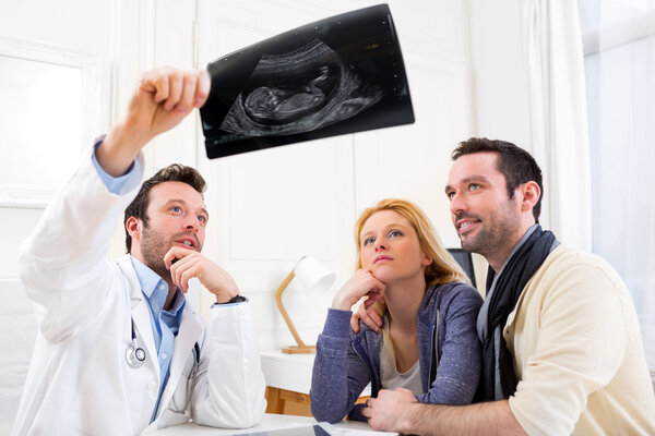 Doctor shows an ultrasound to a young happy couple