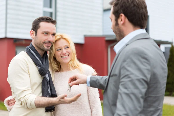 Agente imobiliário entrega chaves para jovem casal atrativo — Fotografia de Stock