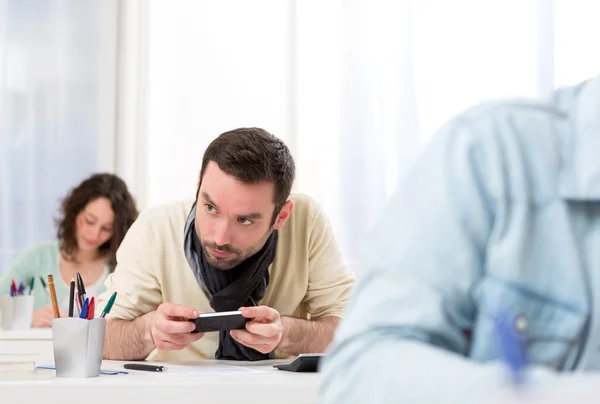 Junger attraktiver Mann betrügt mit Handy während der Prüfung — Stockfoto