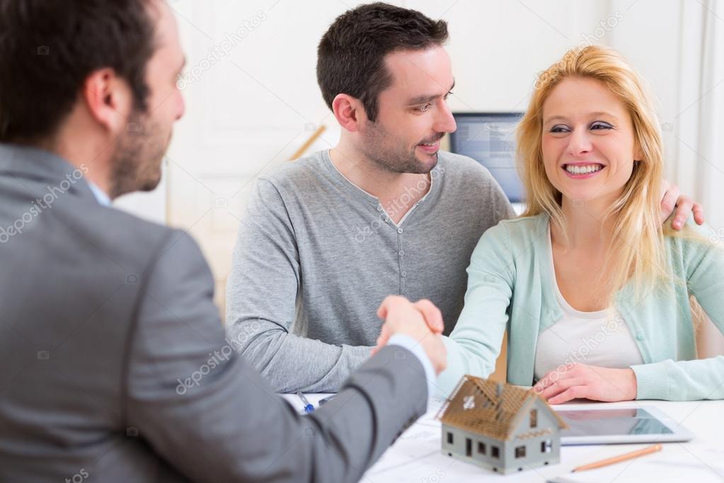 Young happy couple handshaking real estate agent after signing c