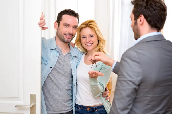 Onroerende goederenagent levert sleutels van nieuw huis aan jong koppel — Stockfoto