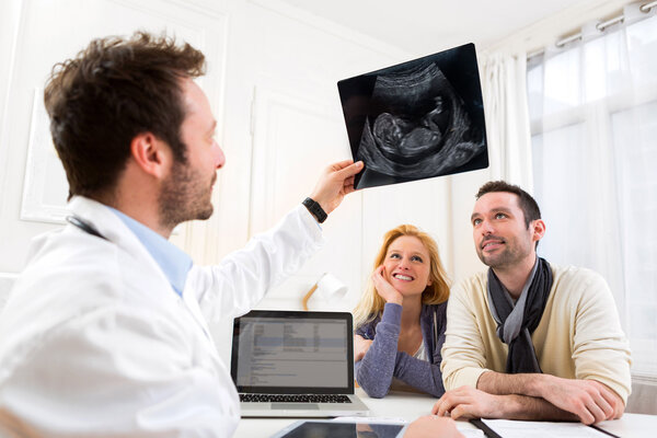 Doctor shows an ultrasound to a young happy couple