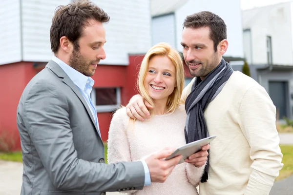 Real estate agent and a young couple in front of their next home — Stock Photo, Image