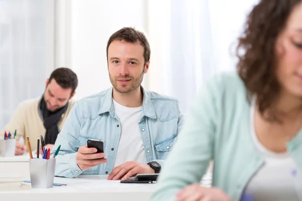 Young attractive student using his mobile during classes — Stock Photo, Image
