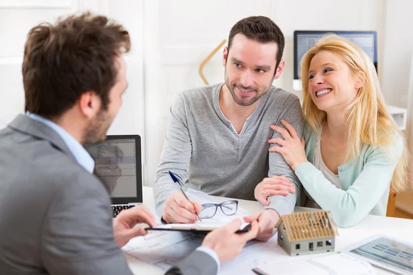 Jeune couple attrayant signant un contrat avec un agent immobilier — Photo