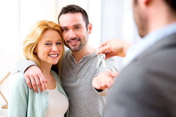 Onroerende goederenagent levert sleutels van nieuw huis aan jong koppel — Stockfoto