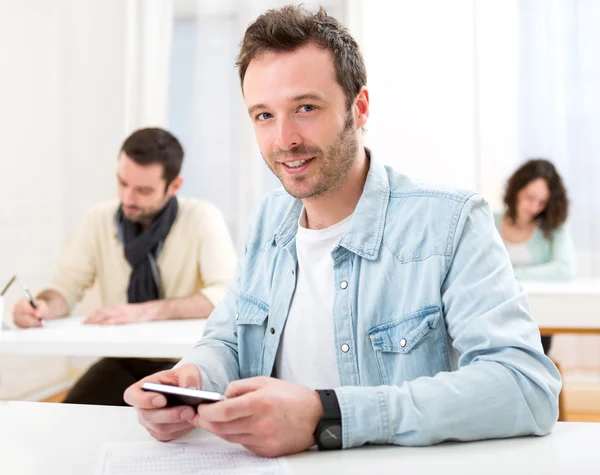 Junger attraktiver Schüler benutzt sein Handy während des Unterrichts — Stockfoto