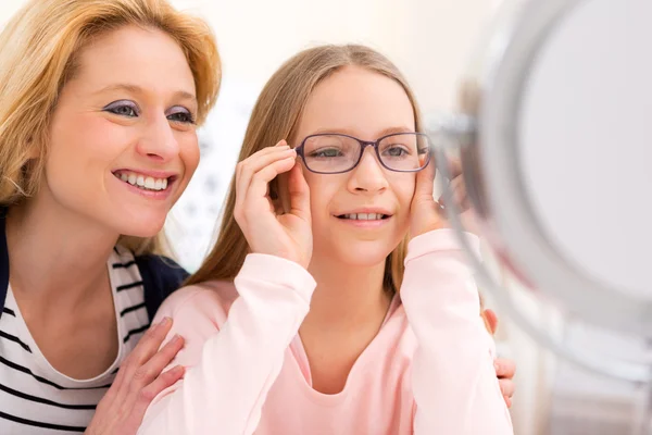 Young little girl trying glasses at the optician w her mother — Stock Photo, Image