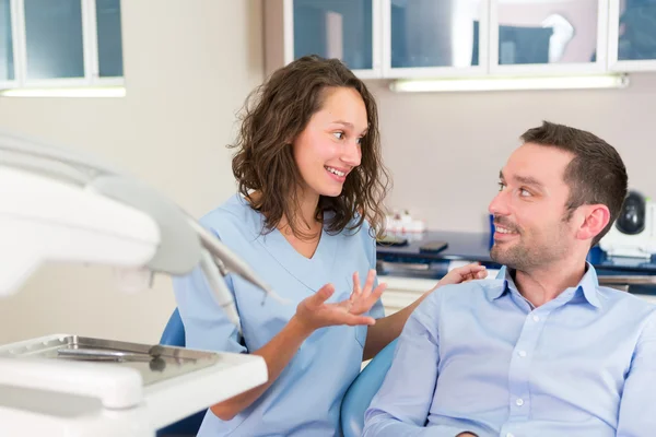 Joven dentista atractivo explicando su trabajo a un paciente — Foto de Stock