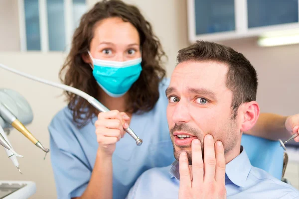 Joven hombre atractivo asustado de ser curado por un dentista — Foto de Stock