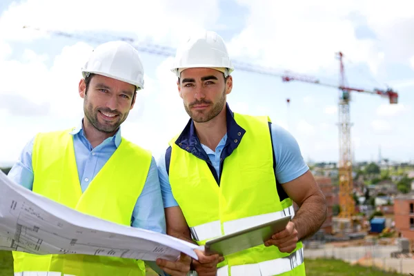 Engineer and worker watching blueprint on construction site — Stock Photo, Image