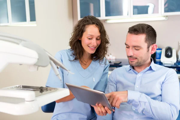 Joven dentista atractivo explicando su trabajo a un paciente — Foto de Stock