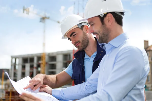 Инженер и рабочий наблюдают за чертежами на строительной площадке — стоковое фото