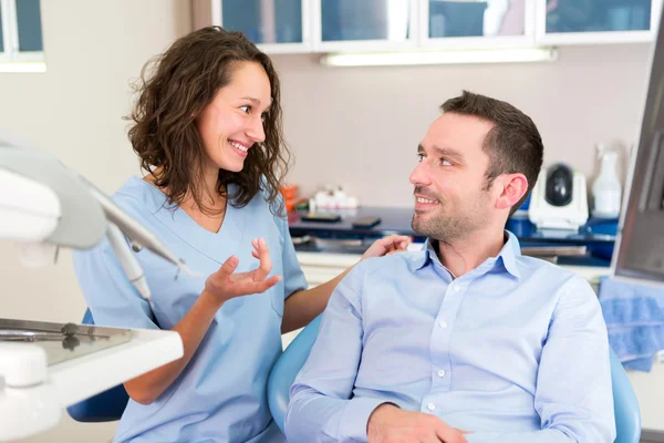 Joven dentista atractivo explicando su trabajo a un paciente — Foto de Stock