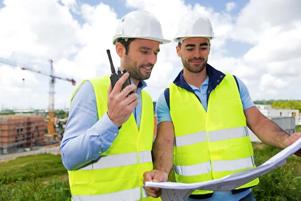 Engineer and worker watching blueprint on construction site — Stock Photo, Image