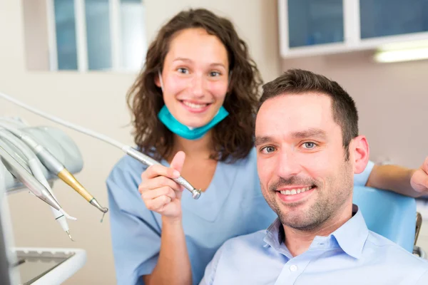 Retrato de un joven dentista atractivo en su consultorio con paciente — Foto de Stock