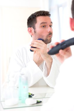 Bir ayna önünde sakalını tıraş genç çekici adam