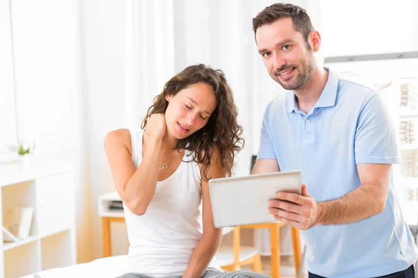 Jonge aantrekkelijke fysiotherapeut tablet met patiënt — Stockfoto