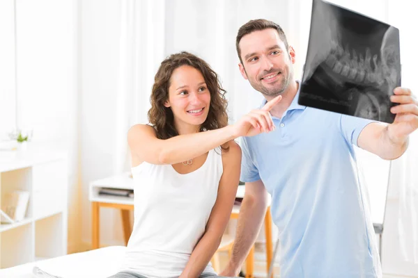 Junge attraktive Physiotherapeutin analysiert Röntgenbild mit Patientin — Stockfoto