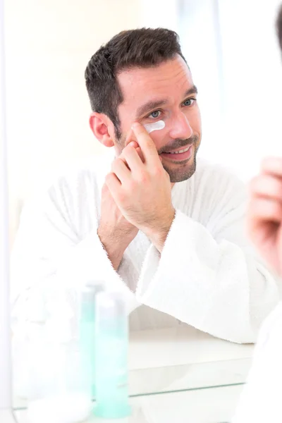 Young attractive man applying anti dark circles cream around eye — Stock Photo, Image