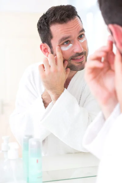 Jovem atraente homem aplicando anti olheiras creme ao redor do olho — Fotografia de Stock