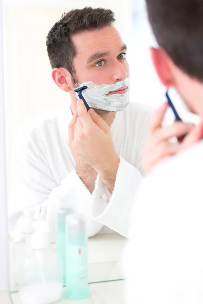 Jeune homme séduisant se rasant la barbe devant un miroir — Photo