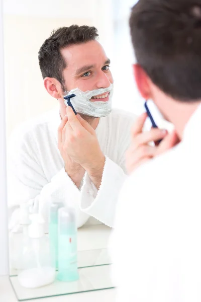 Jeune homme séduisant se rasant la barbe devant un miroir — Photo