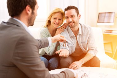 Emlakçı yeni ev anahtarları için genç çift sunar.