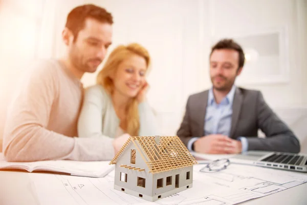 Casa em miniatura em uma mesa de agente imobiliário com casal — Fotografia de Stock